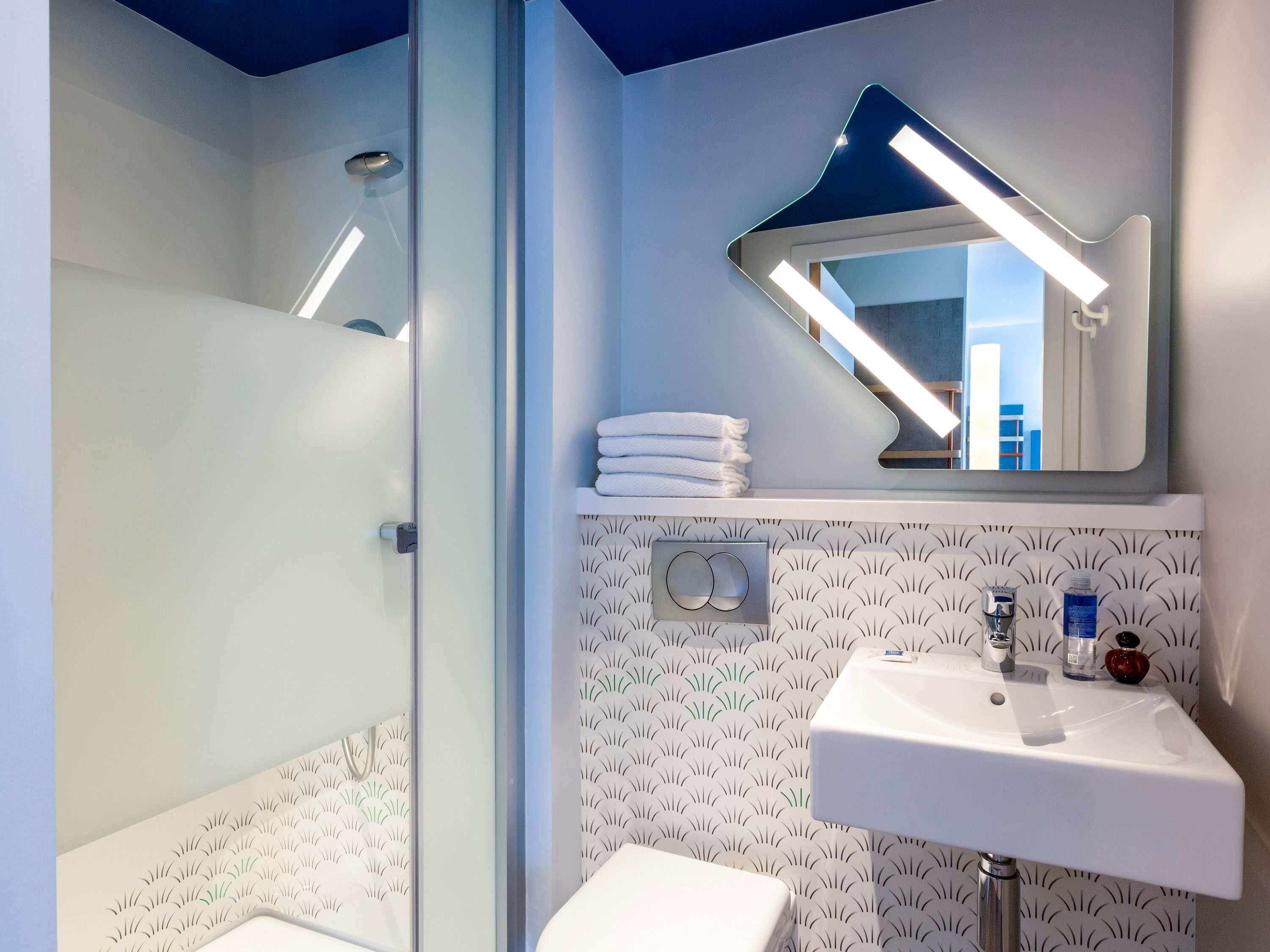 Un baño con cabina de ducha de vidrio, un lavabo blanco con espejo y azulejos decorativos en la pared.