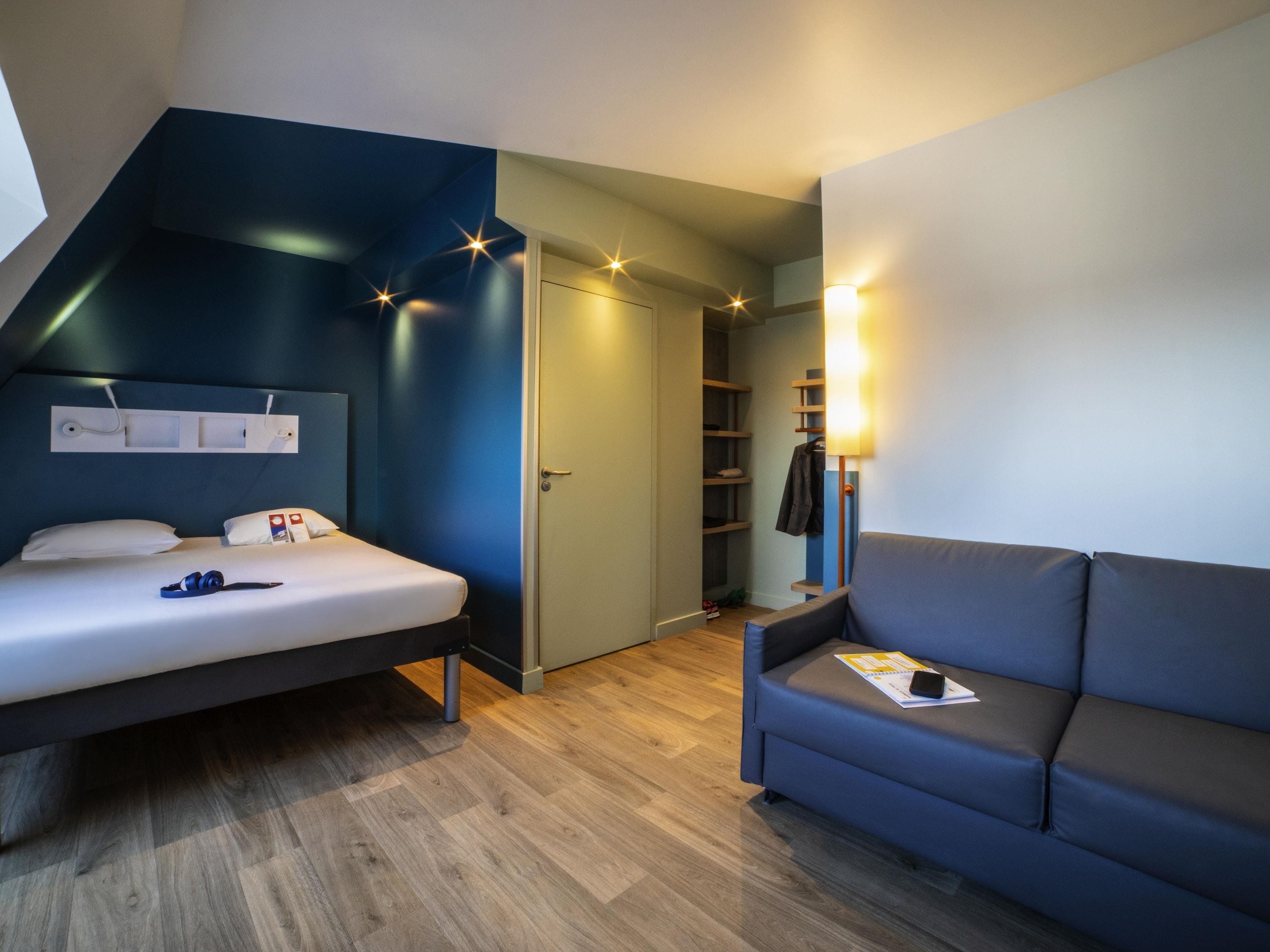 Ein Schlafzimmer mit einem Bett, einer blauen Wand, einem Holzboden, einem Kleiderschrank und einem Nachttisch.