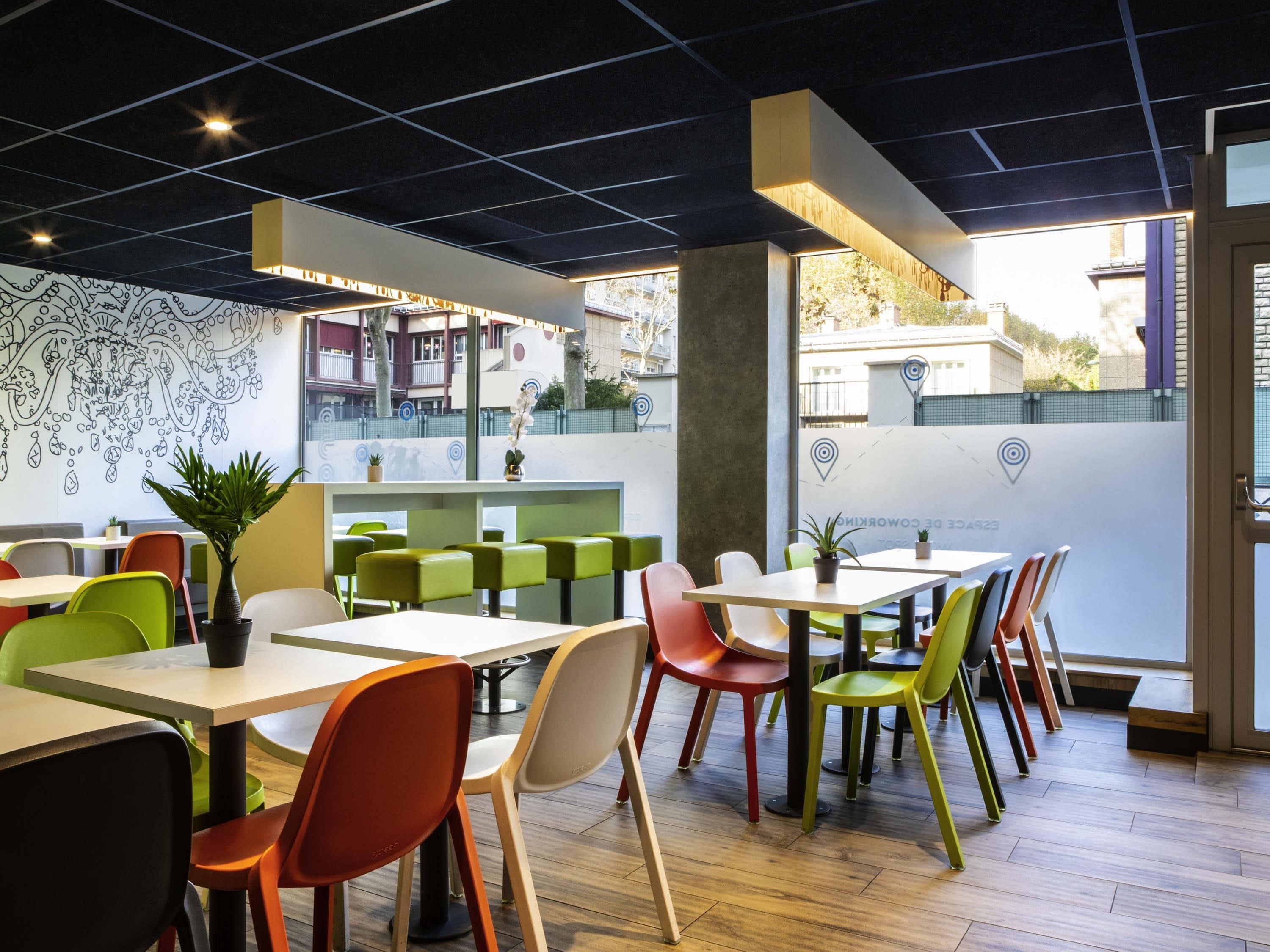 A modern restaurant interior with colorful chairs, tables, and a decorative wall mural.