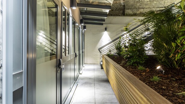 Un bâtiment moderne doté d’une façade en verre, d’un jardinier en bois planté de végétaux et d’un escalier en métal.