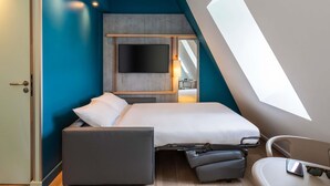 Une chambre moderne avec un lit, un bureau et une chaise. Une grande fenêtre laisse entrer la lumière naturelle.