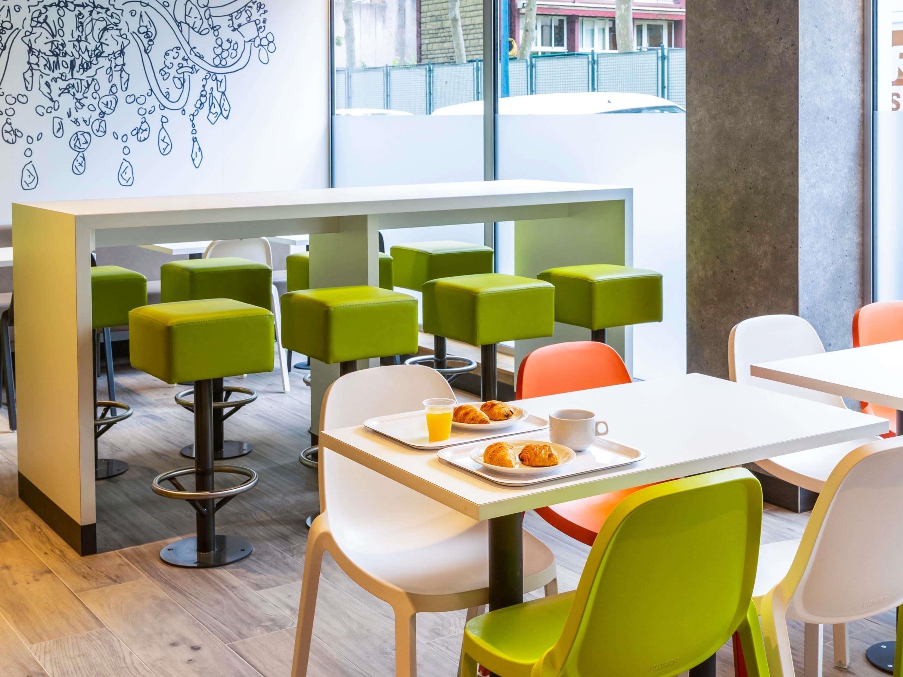 A modern cafe with green and white chairs, a white table, and a tray with croissants and a cup.