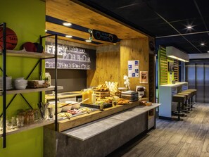 Una zona de buffet amb diversos plats, un menú escrit a la pissarra i tamboretes de bar.