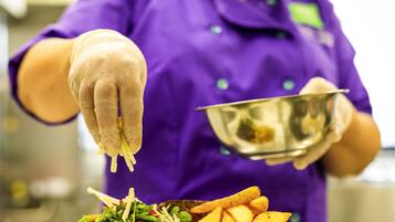 A person in a purple uniform and gloves preparing food, with a plate of fries and salad in the foreground.