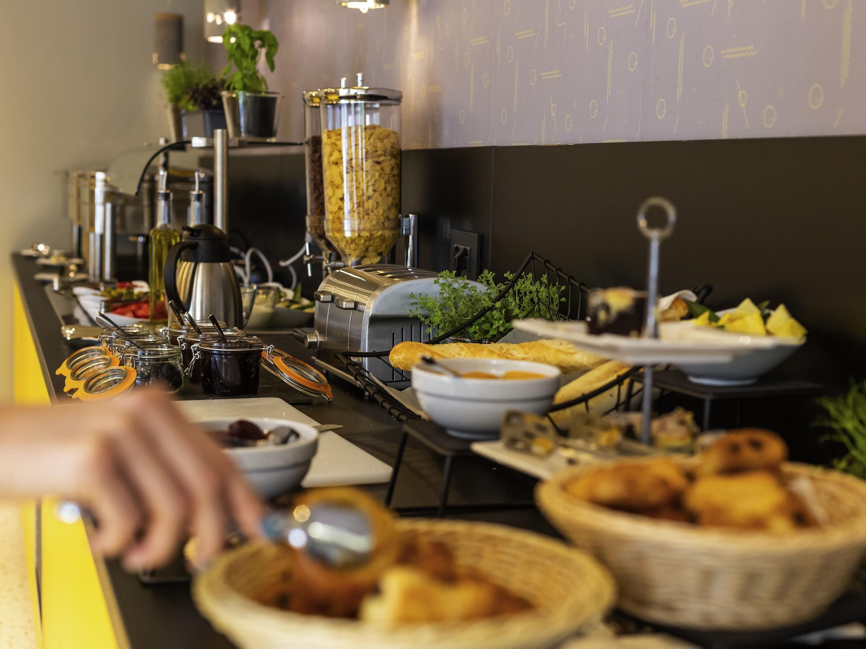 A buffet setup with various food items, including bowls of soup, baskets of bread, and jars of condiments.
