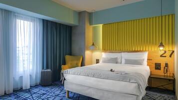 Una habitación de hotel con cama, una silla, una lámpara, una mesita de noche y una ventana con cortinas.
