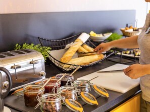 A kitchen counter with a toaster, a basket of bread, and jars of preserves.