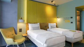 A hotel room with two beds, a chair, a desk, and a wall with a thermostat and a light switch.