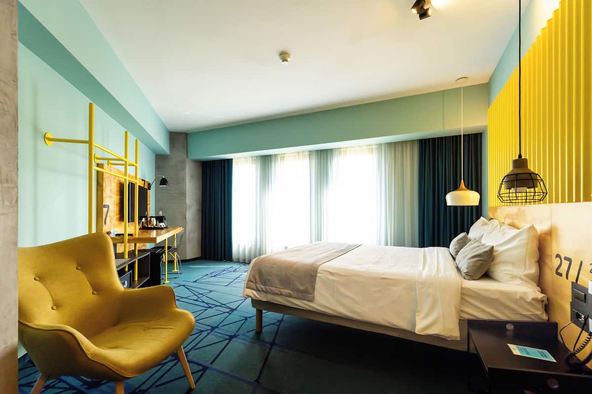 A hotel room with a bed, a chair, a desk, and a lamp.