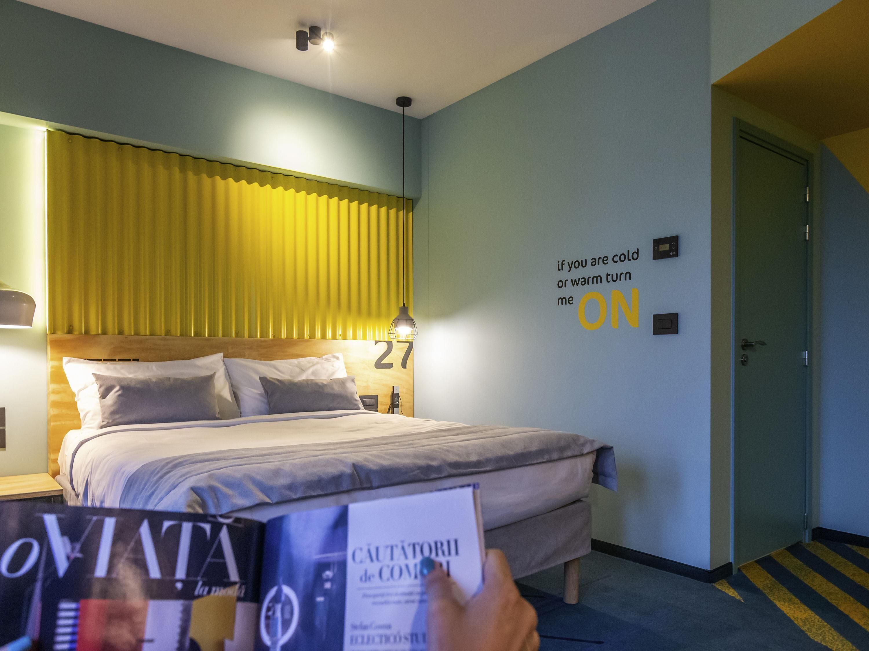 Habitación de hotel con cama, mesita de noche, lámpara y una pared con una cita motivacional.