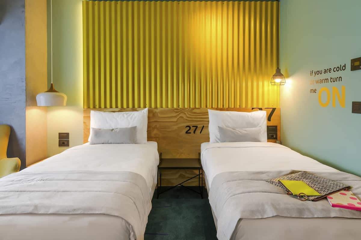 A hotel room with two beds, a headboard with the number 27, a wall with a temperature control sign, and a lamp on the left side.