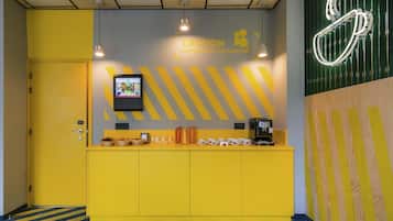 Una zona de recepción con un mostrador amarillo, una máquina de café y un letrero de neón.