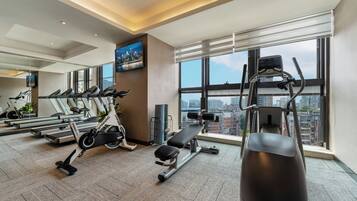A modern gym with treadmills, a spinning bike, and weight equipment, featuring large windows and a city view.