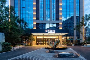 A modern hotel entrance with a glass facade, a sign for 'encore' and 'RAMADA', and a water feature in front. - Ramada Encore Chongqing Yubei (Chongqing)