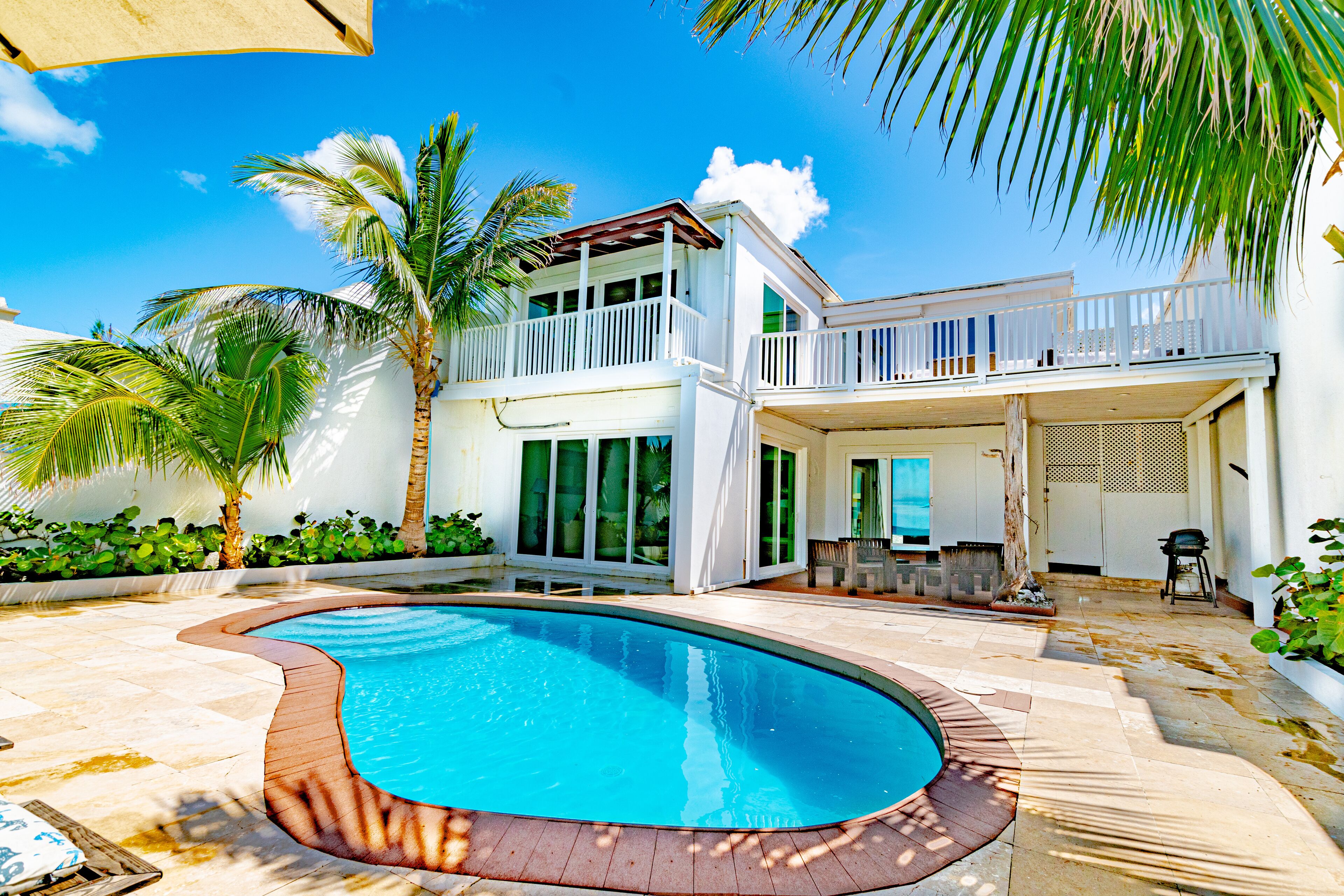 A two-story house with a swimming pool, a balcony, and a patio area with outdoor furniture.