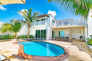 A two-story house with a swimming pool, a balcony, and a patio area with outdoor furniture.