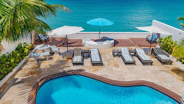 Área de piscina com espreguiçadeiras e guarda-sóis, com vista para um oceano azul e límpido.