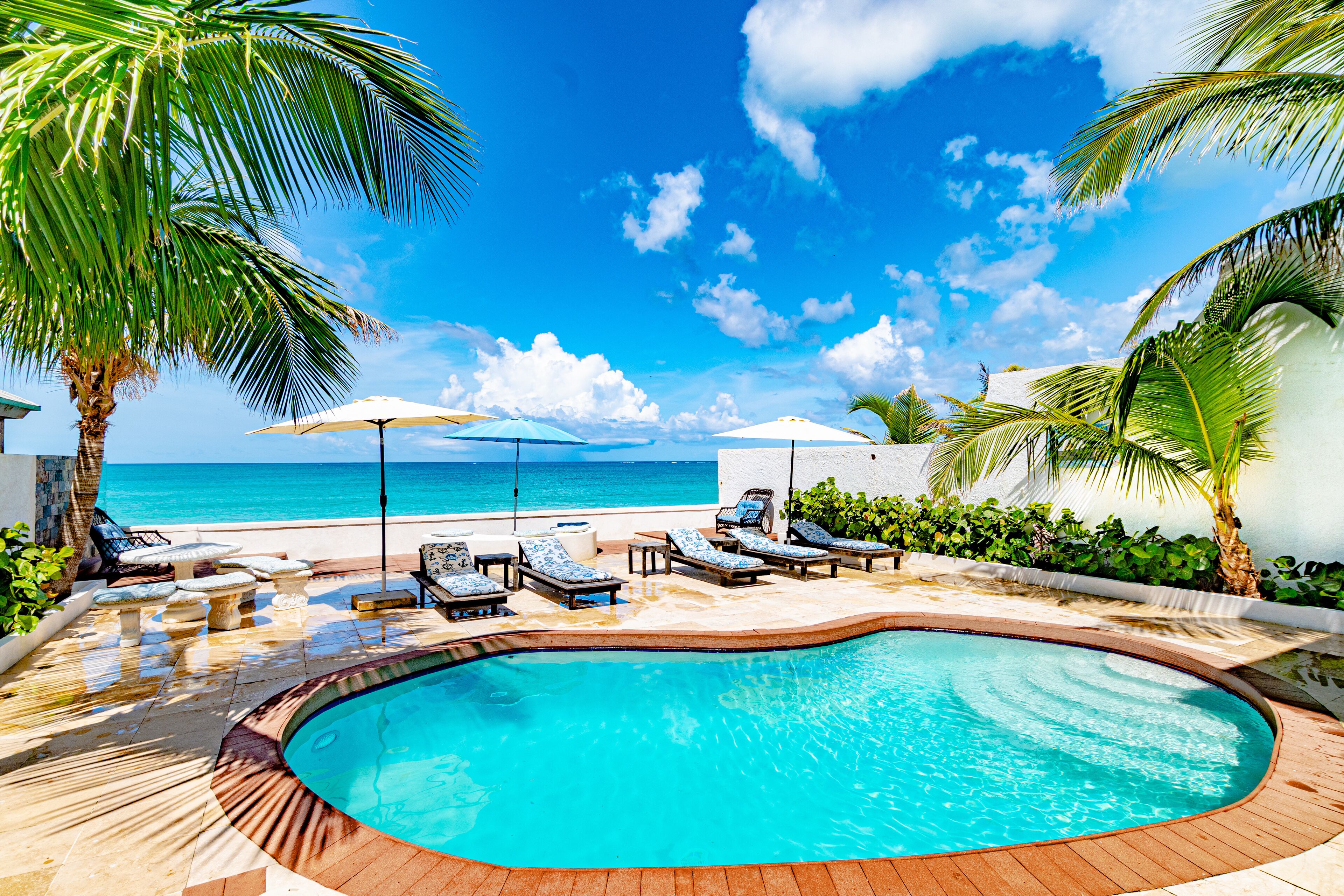 A poolside area with lounge chairs and umbrellas, a pool, and a view of the ocean.