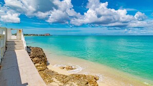 Um caminho costeiro que leva a uma praia com águas turquesa cristalinas e um litoral rochoso.
