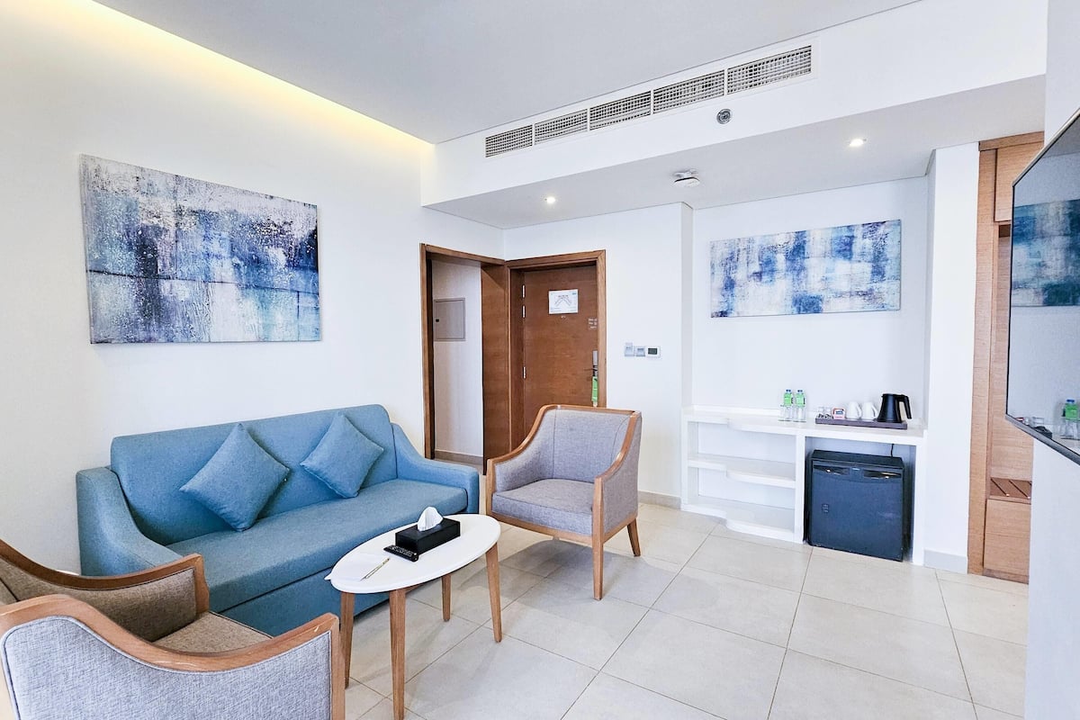 Een moderne woonkamer met een blauwe bank, twee fauteuils, een salontafel en kunst aan de muren.