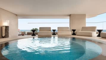 A pool area with lounge chairs and a view of the ocean.