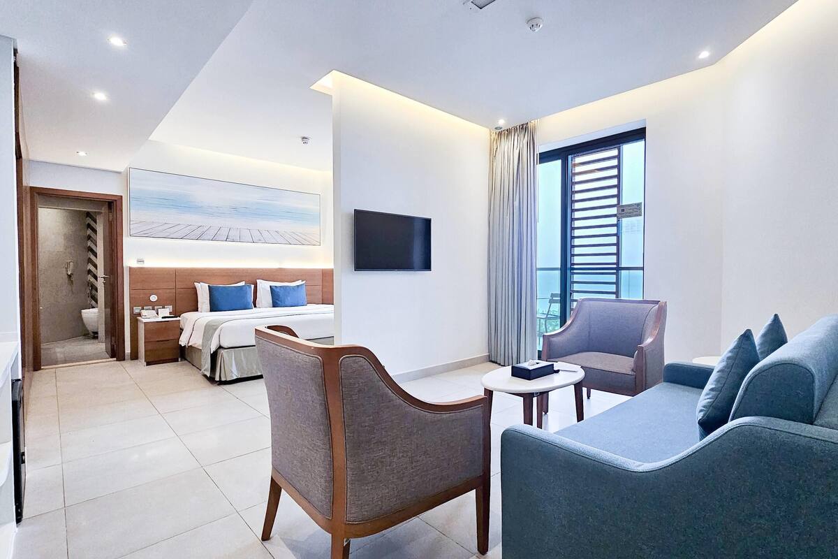 Een hotelkamer met een bed, een televisie, een bank en een stoel. Er is een raam met gordijnen en uitzicht op buiten.