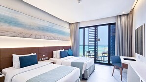 Camera d'albergo con due letti, una scrivania e un'ampia finestra vista spiaggia.