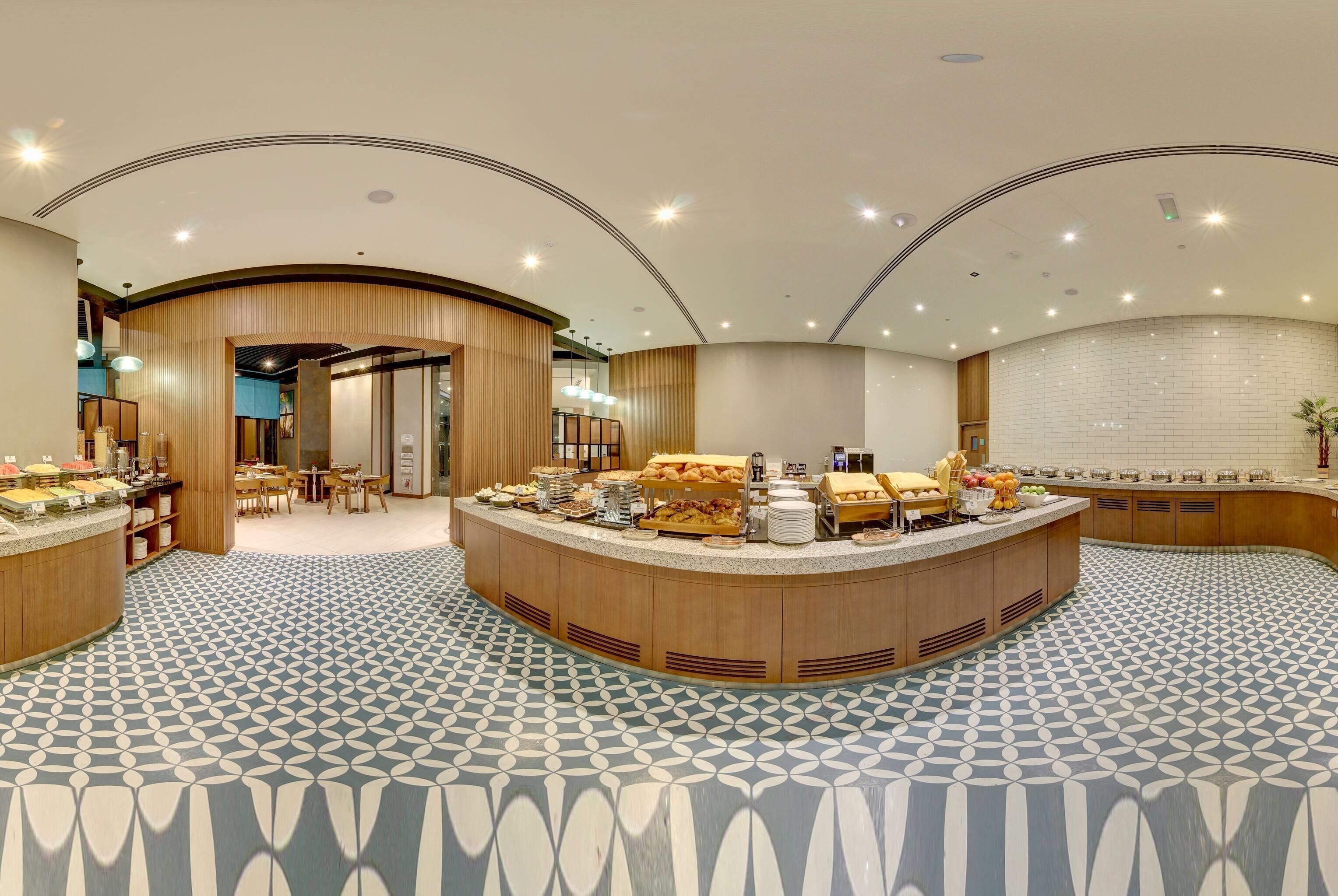 A hotel lobby with a central breakfast bar, seating area, and a patterned floor.