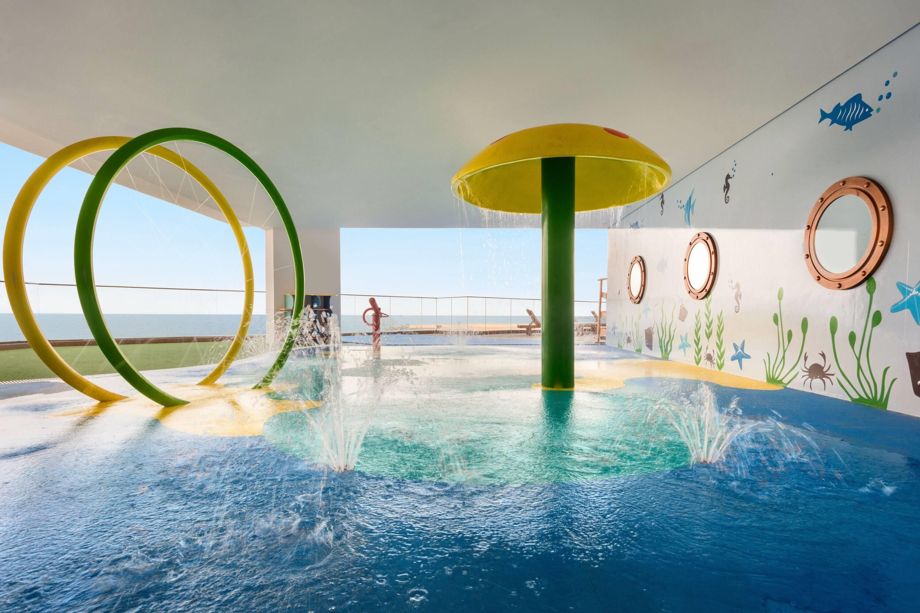 Un espace de jeux aquatiques intérieur doté d’éléments aquatiques circulaires et d’une fresque représentant un paysage sous-marin.