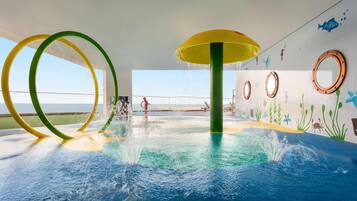 Un espace de jeux aquatiques intérieur doté d’éléments aquatiques circulaires et d’une fresque représentant un paysage sous-marin.