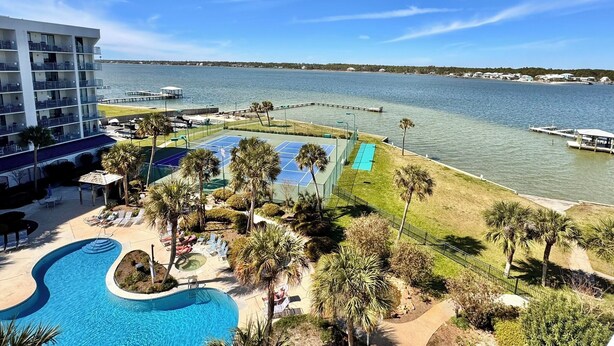 A hotel with a swimming pool, tennis courts, and a view of the water.