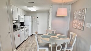 A compact kitchen with white cabinets, a dining table with four chairs, and a hanging pendant light.