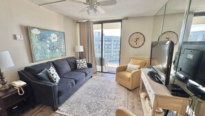 A living room with a sofa, armchair, TV, and a painting on the wall.
