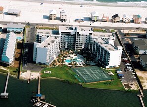 An aerial view of a coastal hotel with multiple buildings, a swimming pool, and a tennis court.