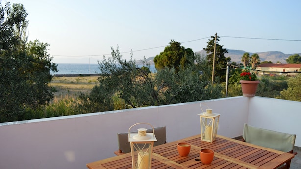 A wooden table with two lanterns and a potted plant on a balcony overlooking a coastal landscape. - Villa Marianthi (Lesvos)