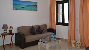 A living room with a sofa, a glass coffee table, a lamp, and a painting of a coastal scene. - Villa Marianthi (Lesvos)