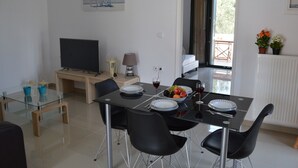 A modern dining area with a glass-top table, black chairs, and a television on a wooden stand. - Villa Marianthi (Lesvos)