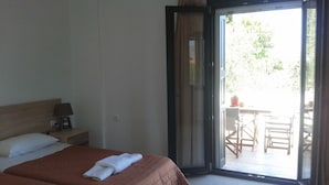 A hotel room with two beds, a nightstand with a lamp, and a sliding glass door leading to an outdoor seating area. - Villa Marianthi (Lesvos)