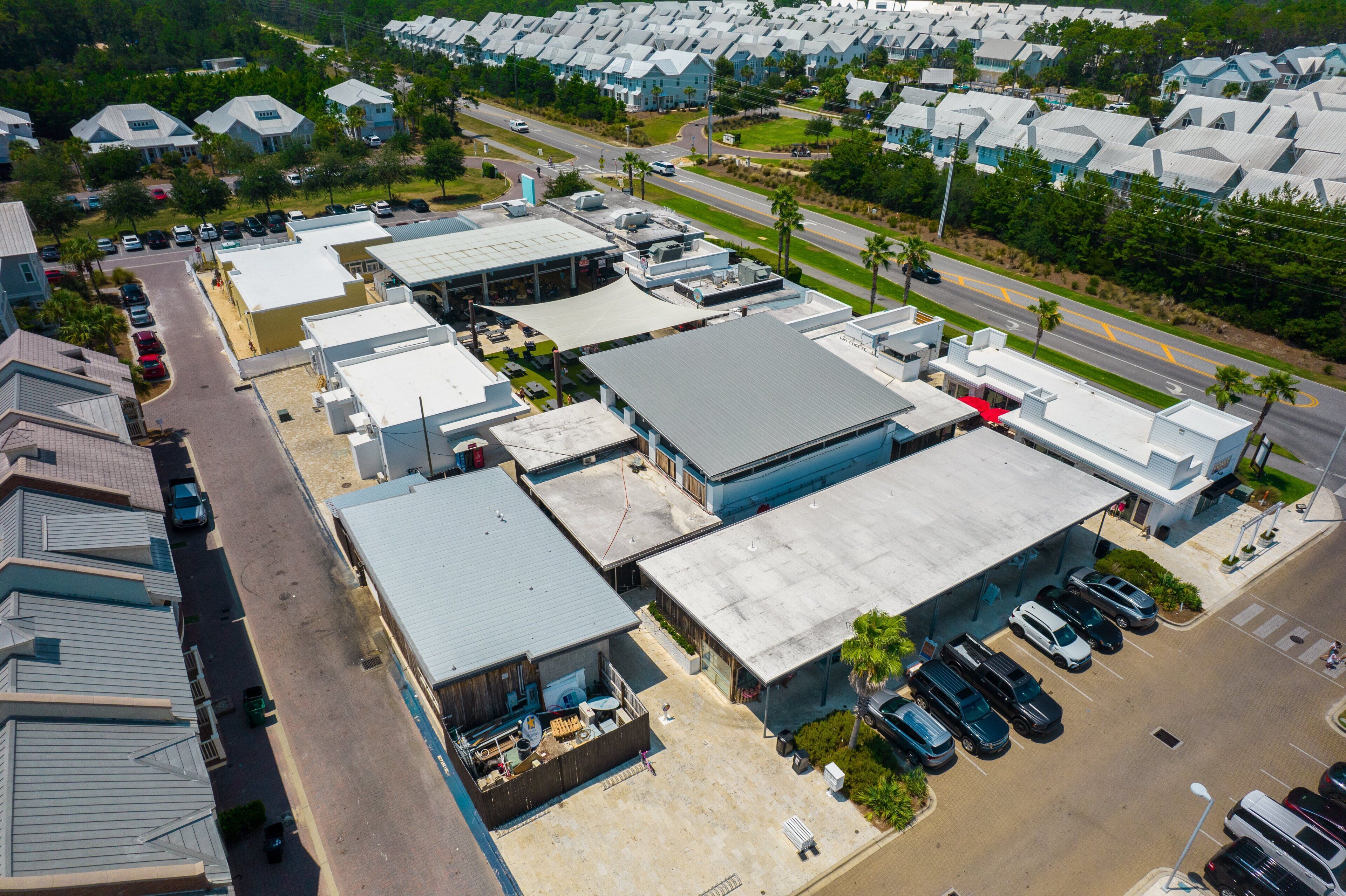Une vue aérienne d’une zone commerciale comprenant plusieurs bâtiments, des parkings et une route.