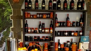 A bar area with shelves of wine bottles, jars of preserves, and a coffee maker.