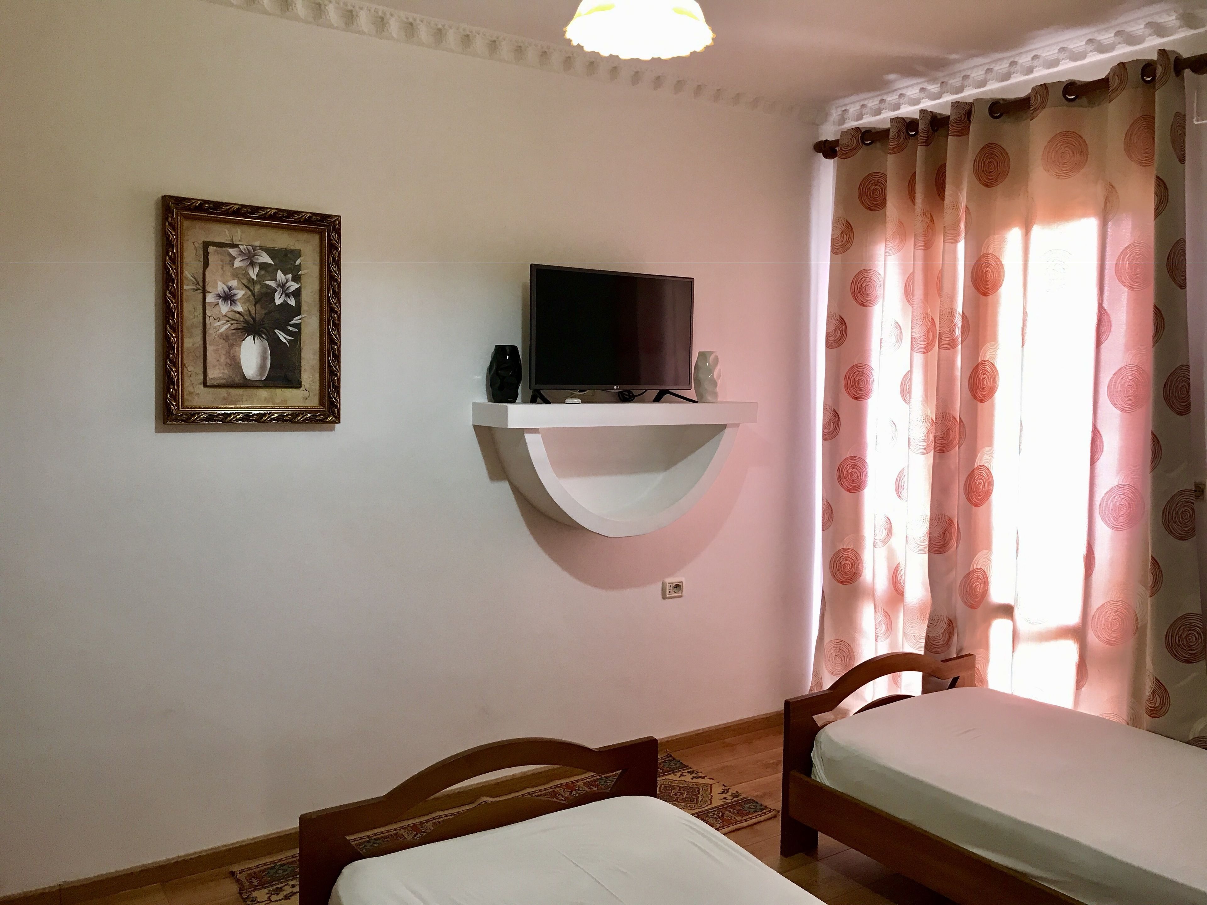 Quarto com cama, televisão montada na parede, quadro emoldurado e janela com cortinas estampadas.