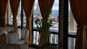 Un comedor con una mesa preparada para dos, una planta en maceta y vistas a una torre a través de amplios ventanales.