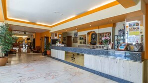 Un vestíbulo de hotel con mostrador de recepción, zona de estar y una planta grande en maceta.