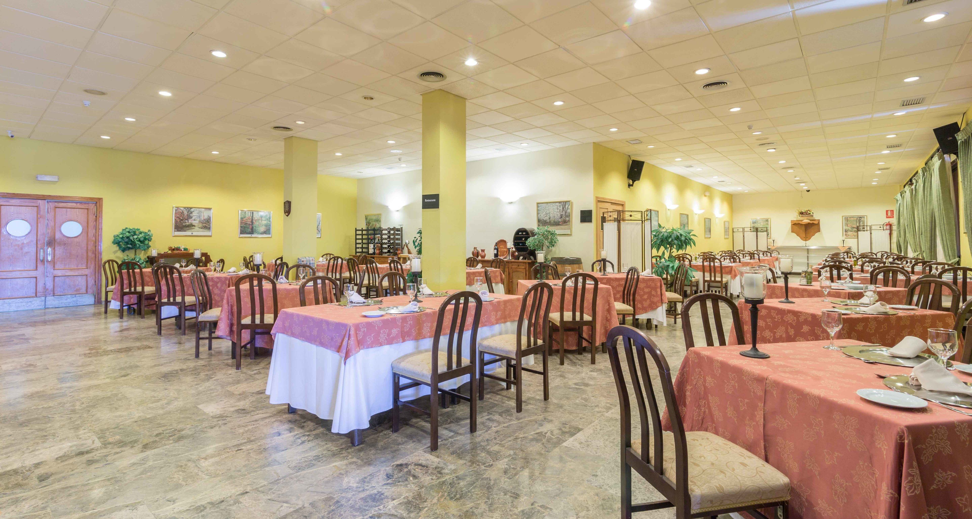 A spacious dining hall with multiple tables and chairs, yellow walls, and a tiled floor.