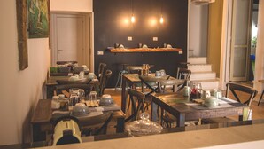 Un comedor con mesas y sillas de madera, lámparas colgantes y una estantería con vajilla.