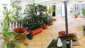 Un patio cubierto con plantas en macetas, muebles de mimbre y suelo de baldosas.