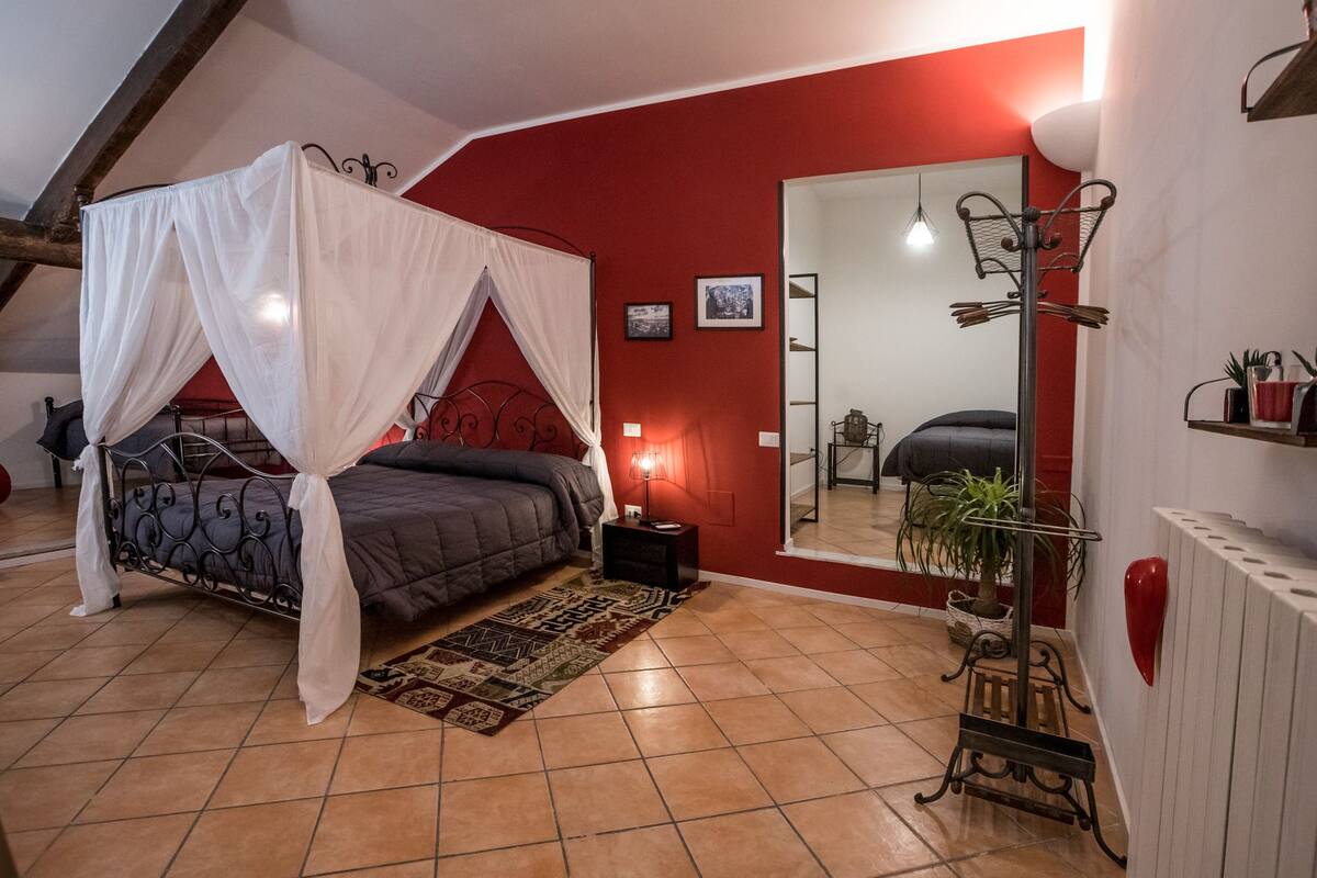 Ein Schlafzimmer mit einem Bett, einem Spiegel, einem Nachttisch und einer roten Wand.