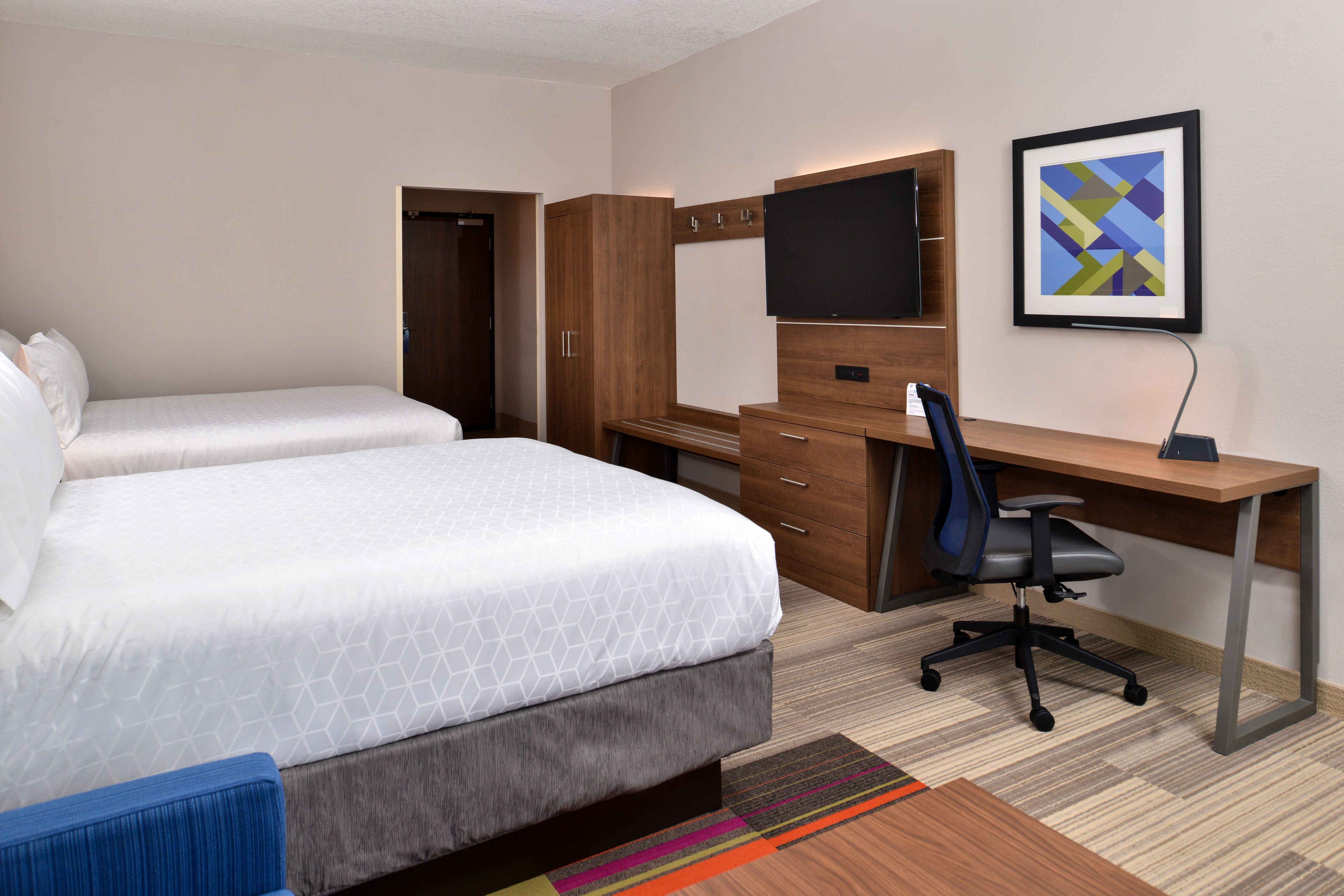 A hotel room with a bed, a desk, a chair, a TV, and a framed picture on the wall.