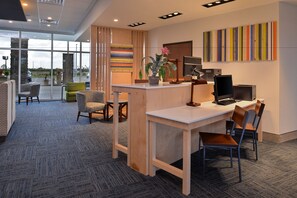 A modern office space with a reception desk, several chairs, a large window, and a colorful abstract painting on the wall. - Holiday Inn Express & Suites Alachua - Gainesville Area by IHG (Alachua)
