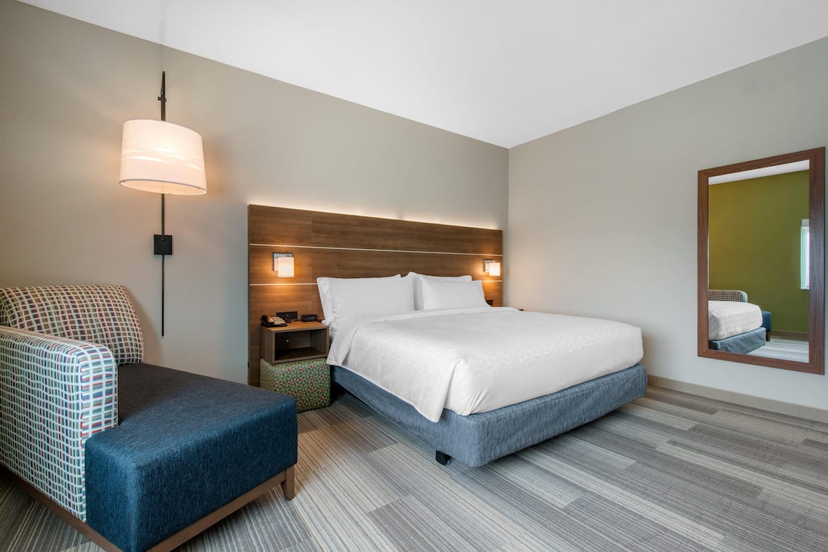 A hotel room with a bed, a chair, a nightstand, a lamp, and a mirror.
